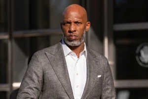 Chauncey Billups in a gray suit and white shirt standing outdoors, looking serious in the sunlight