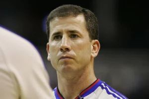 Close-up of a basketball referee wearing a gray uniform with blue and red trim, looking forward during a game