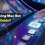 Close-up of a person pressing the “Max Bet” button on a slot machine with text overlay reading “Does Playing Max Bet Increase Odds?” and GamblingNerd branding.