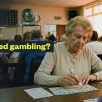 Elderly woman marking a bingo card at a community hall while other players sit behind her; overlay text reads “Is bingo considered gambling?” with GamblingNerd branding.