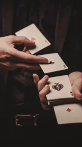 Close-up of a magician performing a card trick, holding multiple aces in their hands against a dark background.