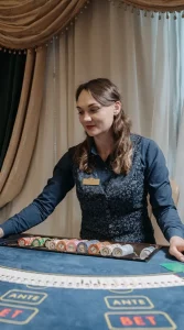 Female casino dealer arranging poker chips at a live gaming table with betting layout visible in an elegant casino setting.
