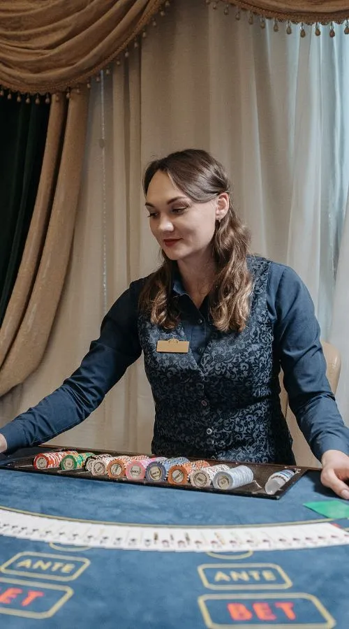 Female casino dealer arranging poker chips at a live gaming table with betting layout visible in an elegant casino setting.