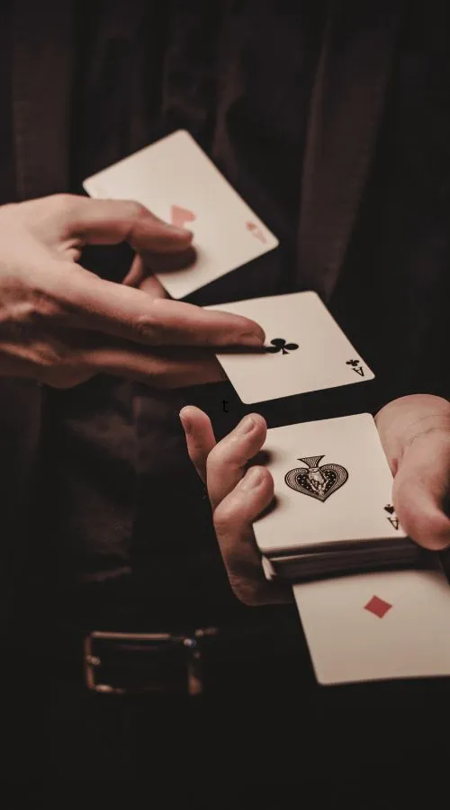 Close-up of a magician performing a card trick, holding multiple aces in their hands against a dark background.