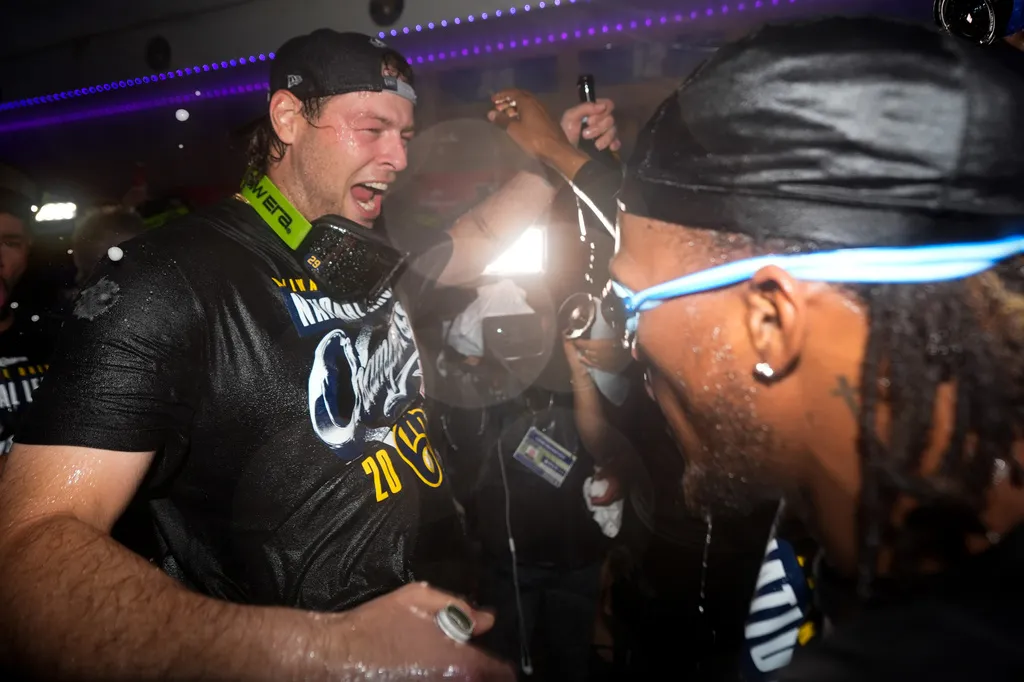 Milwaukee Brewers players celebrate in the clubhouse, wearing goggles and spraying drinks.