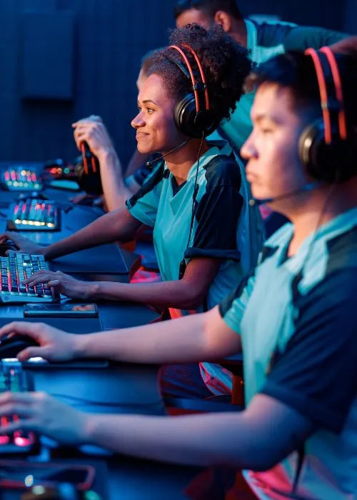 Esports players wearing headsets and matching jerseys compete at desktop computers with illuminated keyboards.