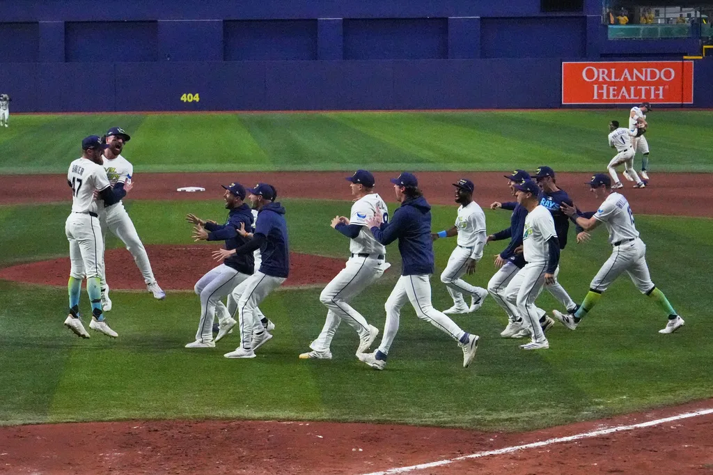 Tampa Bay Rays players celebrate on the field, jumping and running toward teammates.